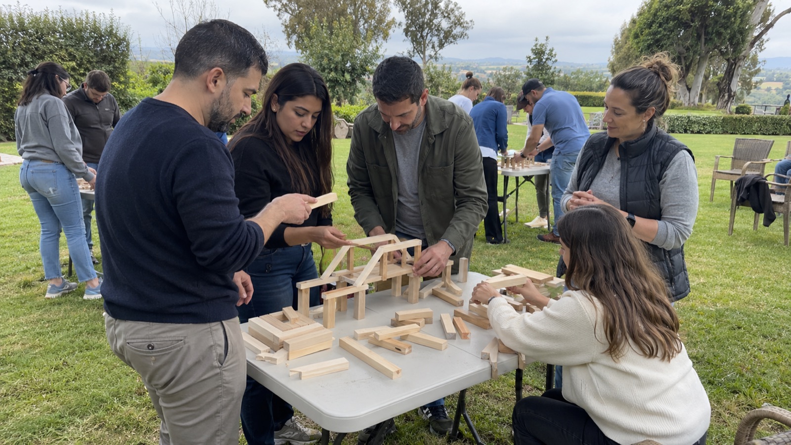 Colleagues building a small bridge together from wooden pieces during a team activity in a hotel garden