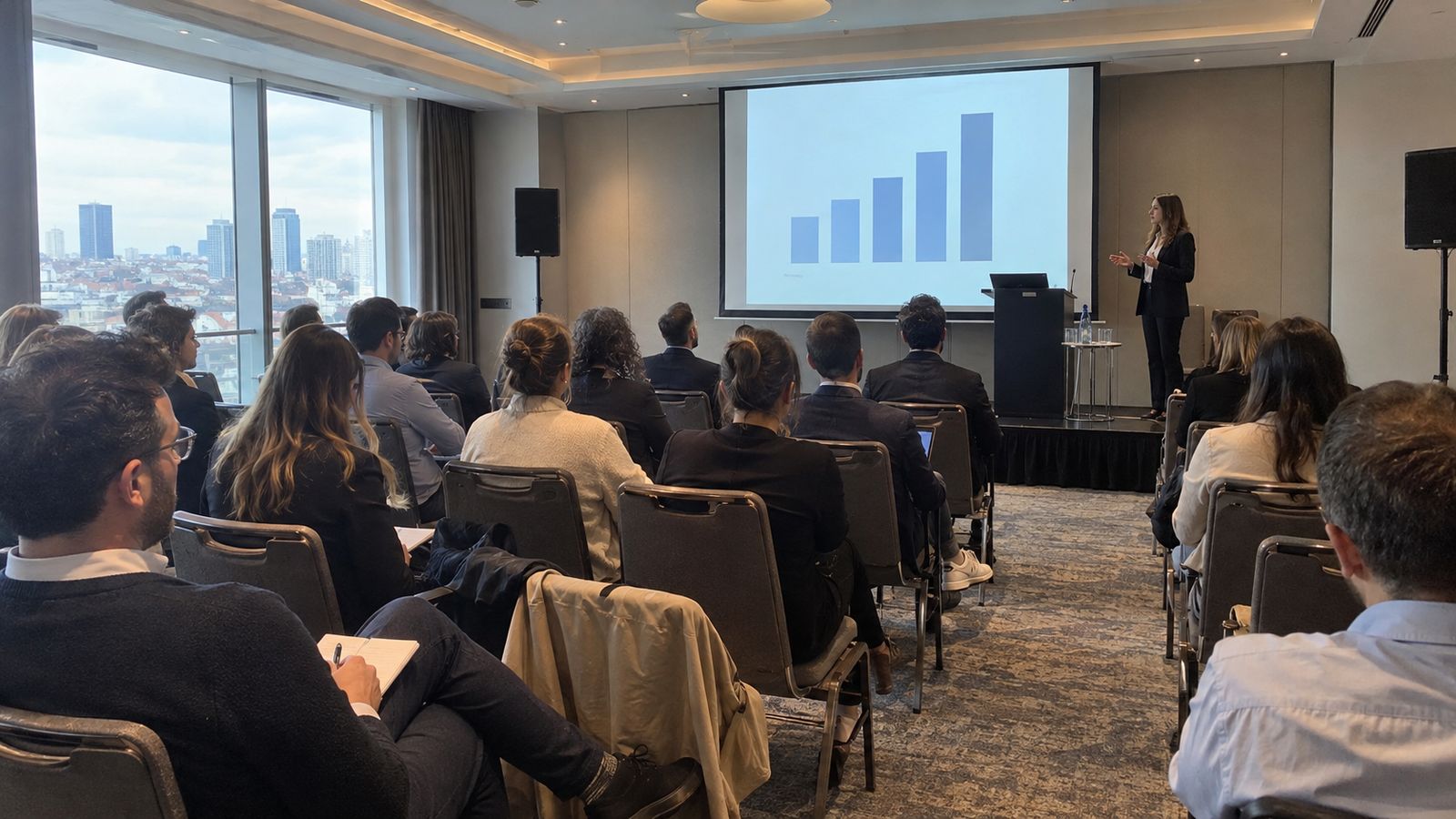 Corporate event attendees listening to a presentation in a hotel conference room.