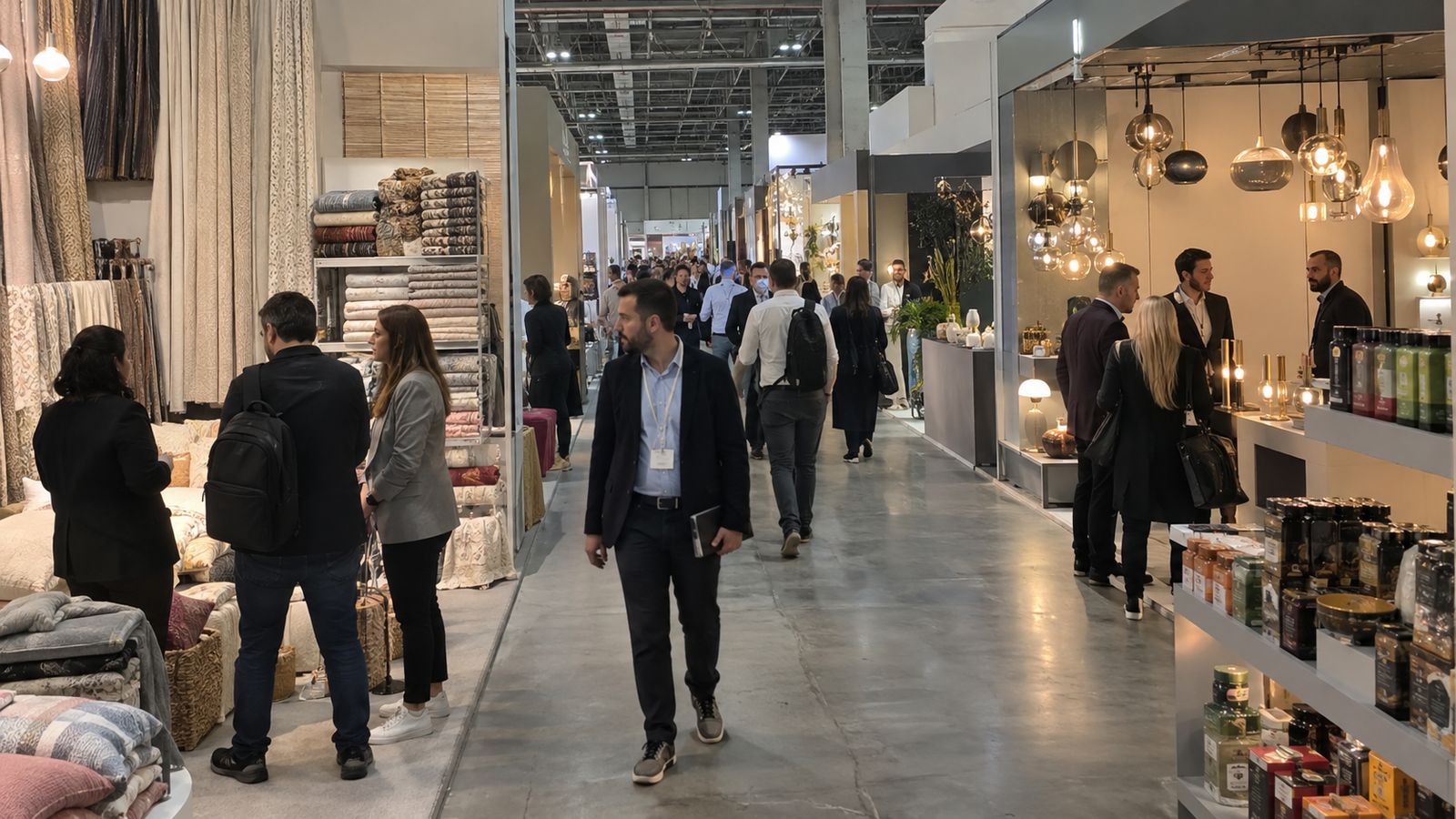 Business visitors walk along a wide exhibition aisle lined with different stands.