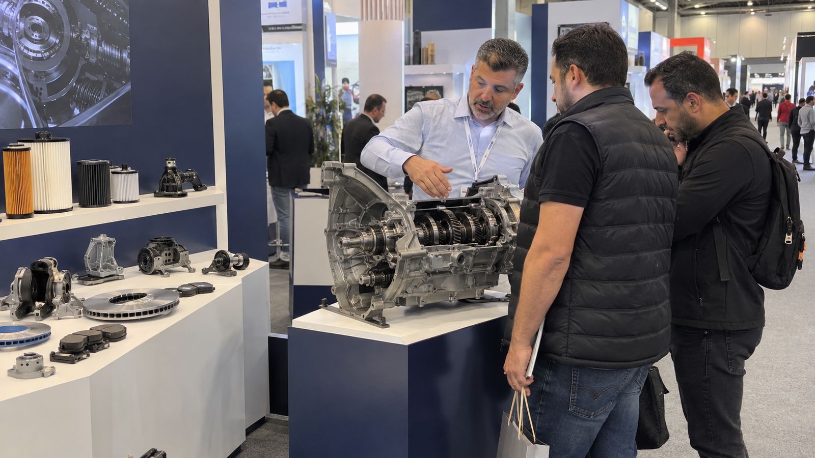 Visitors examining engine components and filters at an automotive exhibition stand