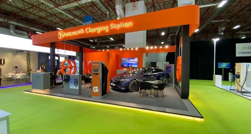 Electric vehicle, charging units and meeting tables within an orange-framed exhibition stand