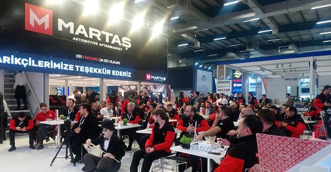 Attendees seated at tables facing a presentation screen within an exhibition stand